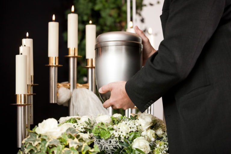 Urne in der Hand eines Manns vor Kerzen und Blumen